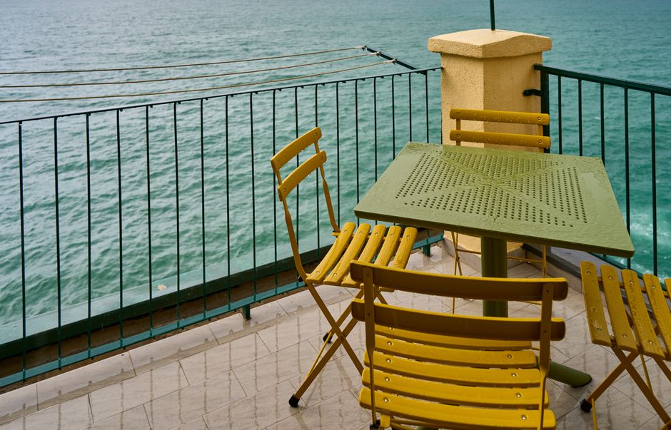 Yellow bistro chairs and table on a seaside balcony overlooking turquoise waters.