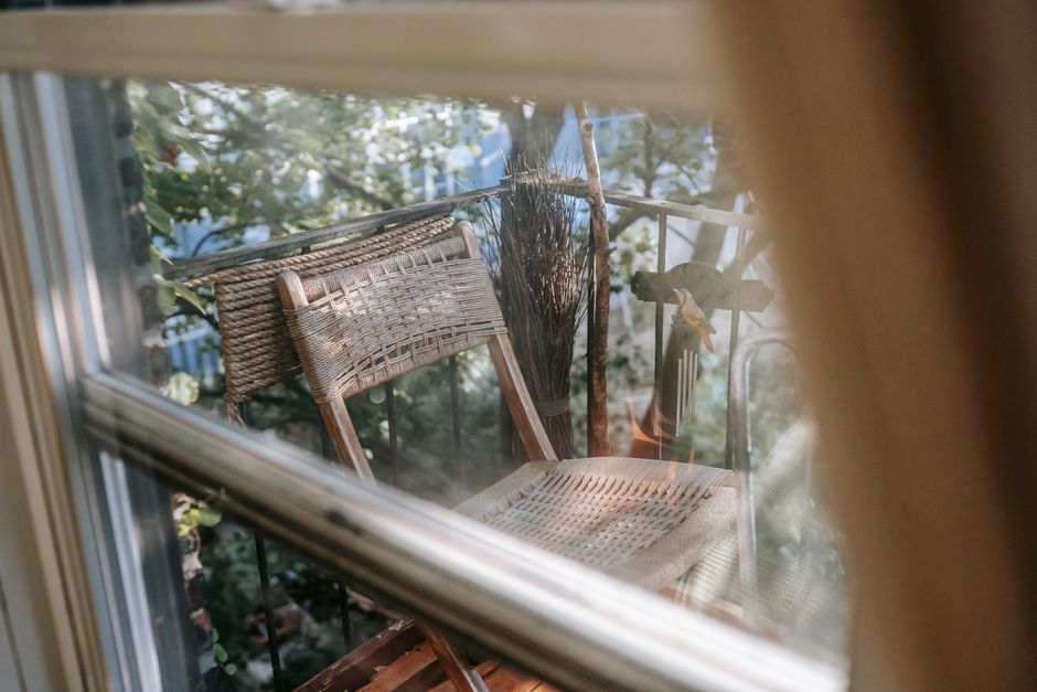 Through glass view of aged cane chair on fenced balcony in countryside house in daylight