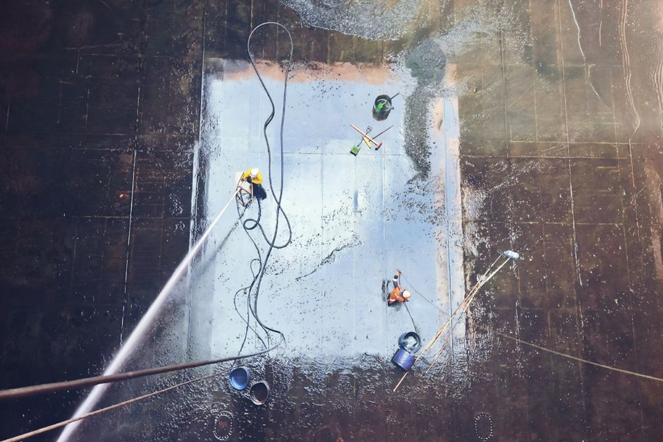 Top view of workers cleaning a large surface with equipment and water hoses.